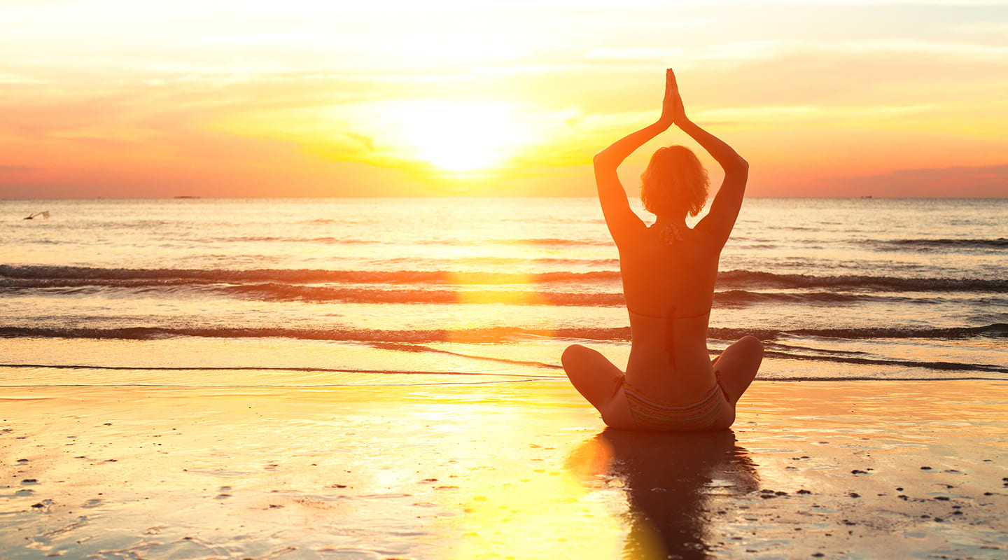 Junge Frau praktiziert Yoga am Strand bei Sonnenuntergang