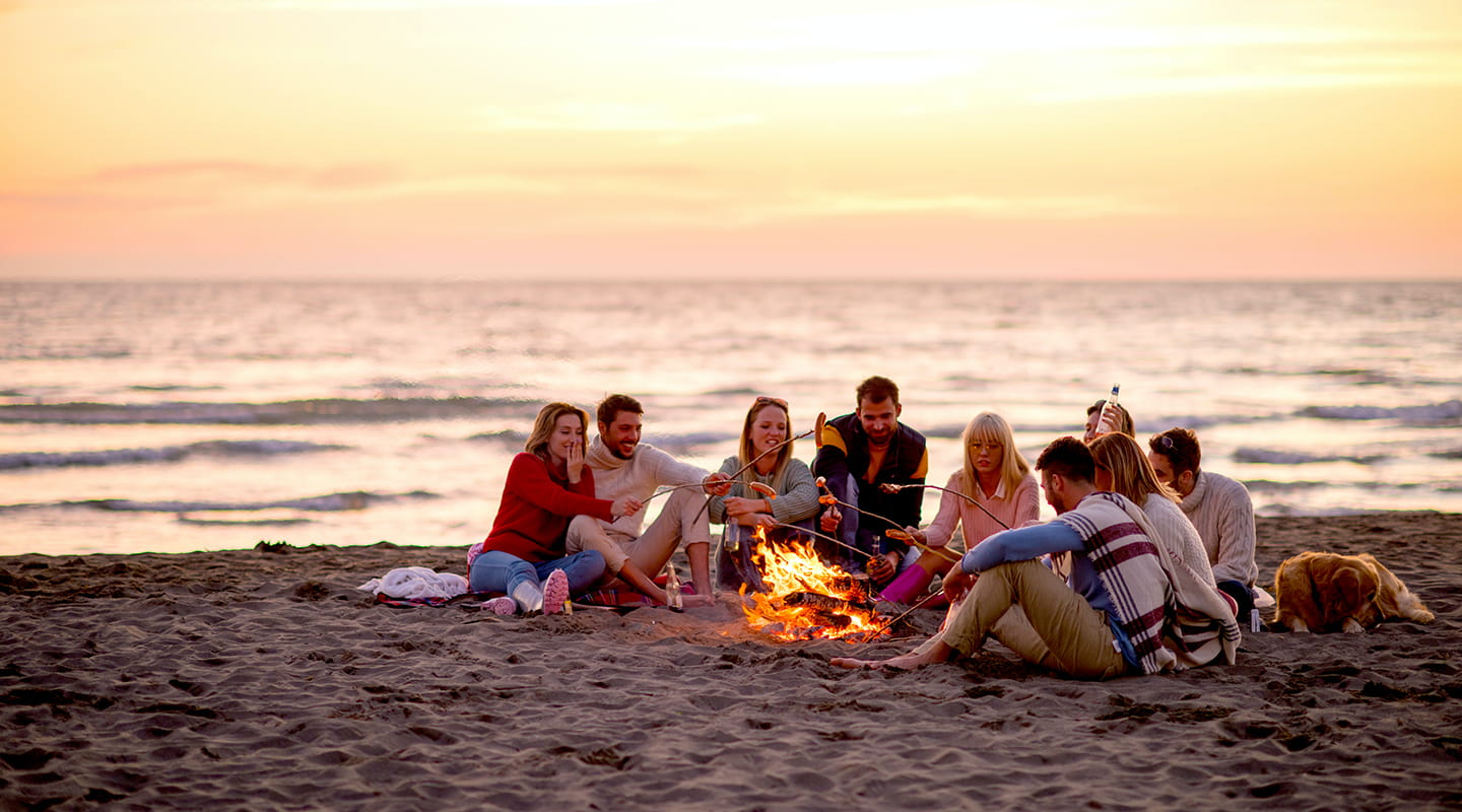 Gruppe von Freunden sitzen abends am Lagerfeuer am Ostseestrand