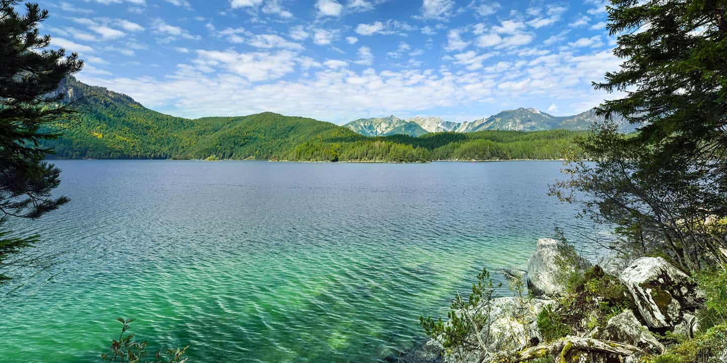 Aussicht auf das grüne Wasser des Eibsees in den Bayerischen Alpen bei der Zugspitze unter dem blauen Himmel mit Wolken