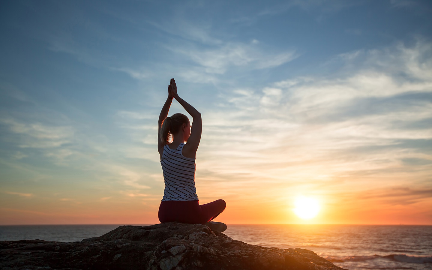 Reisende beim Meditieren im Wellnessurlaub am Meer bei Sonnenuntergang