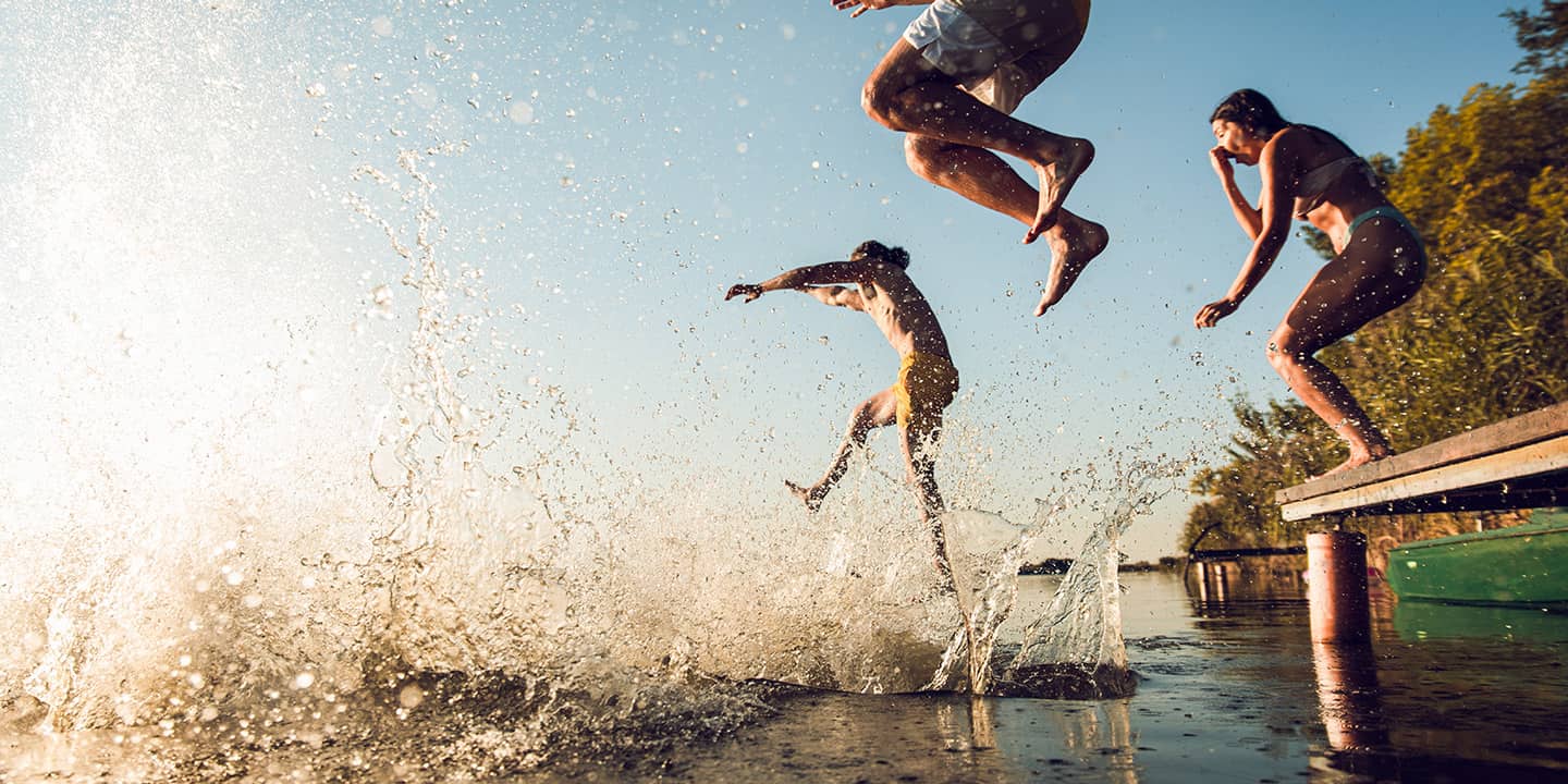 Freunde springen gemeinsam in den See an einem heißen Sommertag