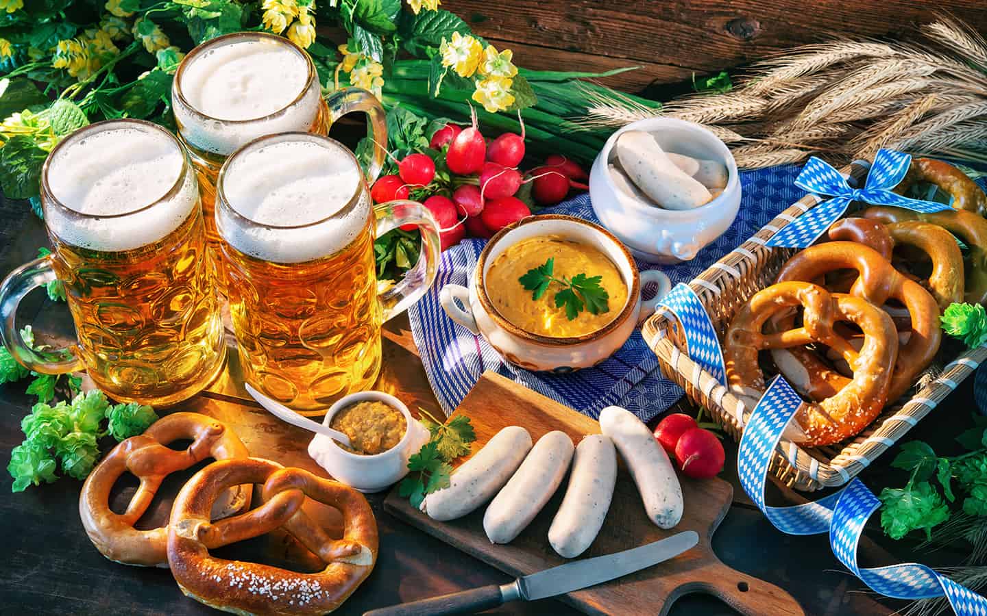 Bayerische Würstchen mit Brezeln, süßem Senf und Bierrümpfe auf rustikalem Holztisch. Oktoberfest-Menü