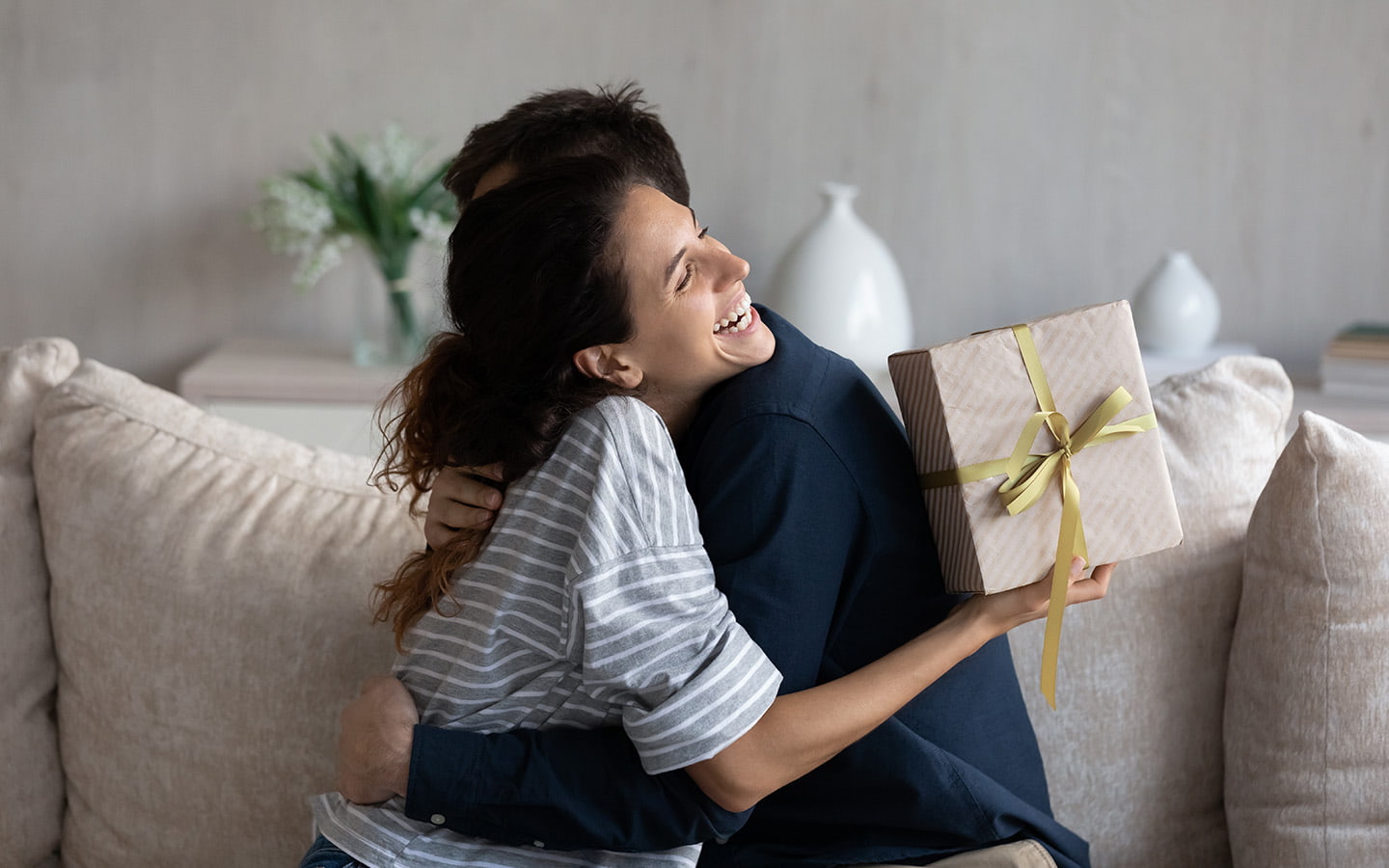 Glückliche junge Frau bekommt einen Reisegutschein in einer Geschenkbox von ihrem Mann überreicht