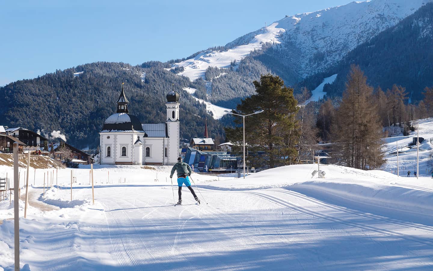Ski-Langläufer auf sonniger Strecke, typisch österreichische Kirche Seefeld, Österreich