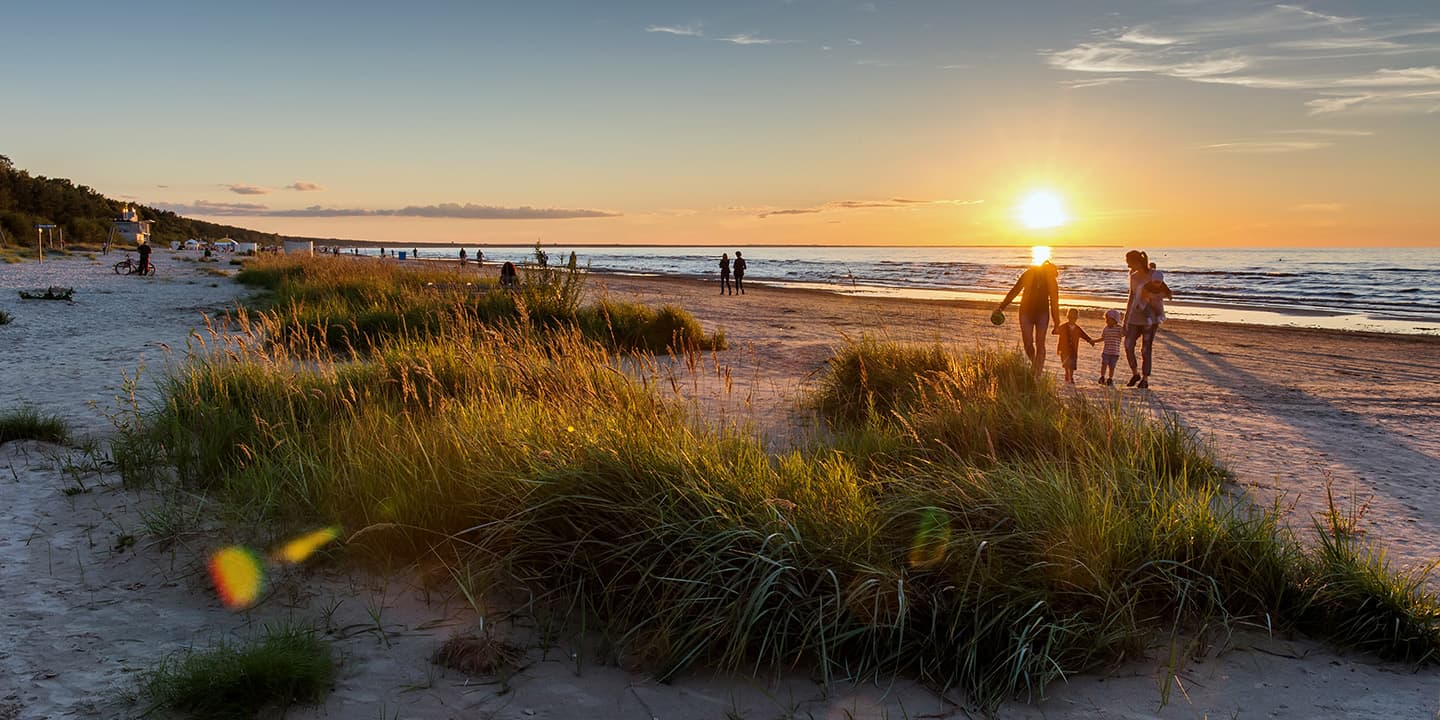 Warmer Sommersonnenuntergang. Strandlandschaft mit Silhouetten von Menschen, Ostsee