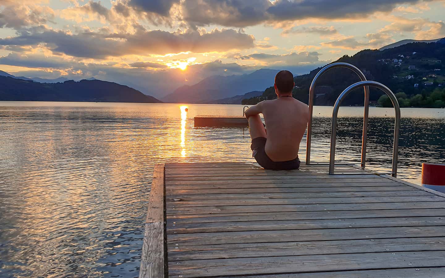 Ein Mann sitzt auf einem Holzsteg am Millstaetter See und genießt den Sonnenuntergang