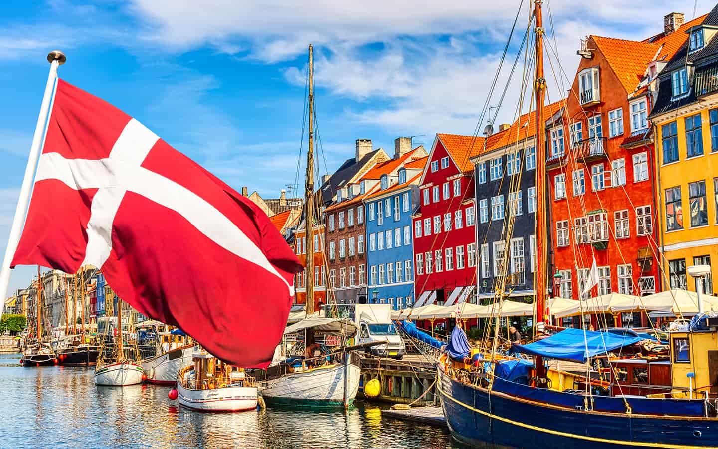 Berühmter alter Nyhavn Hafen im Zentrum von Kopenhagen, Dänemark im Sommer sonnigen Tag mit dänischer Flagge im Vordergrund